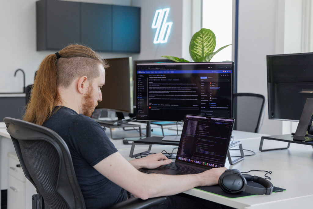Picture of a web developer at a desk in a modern web development agency setting with two monitors working on code