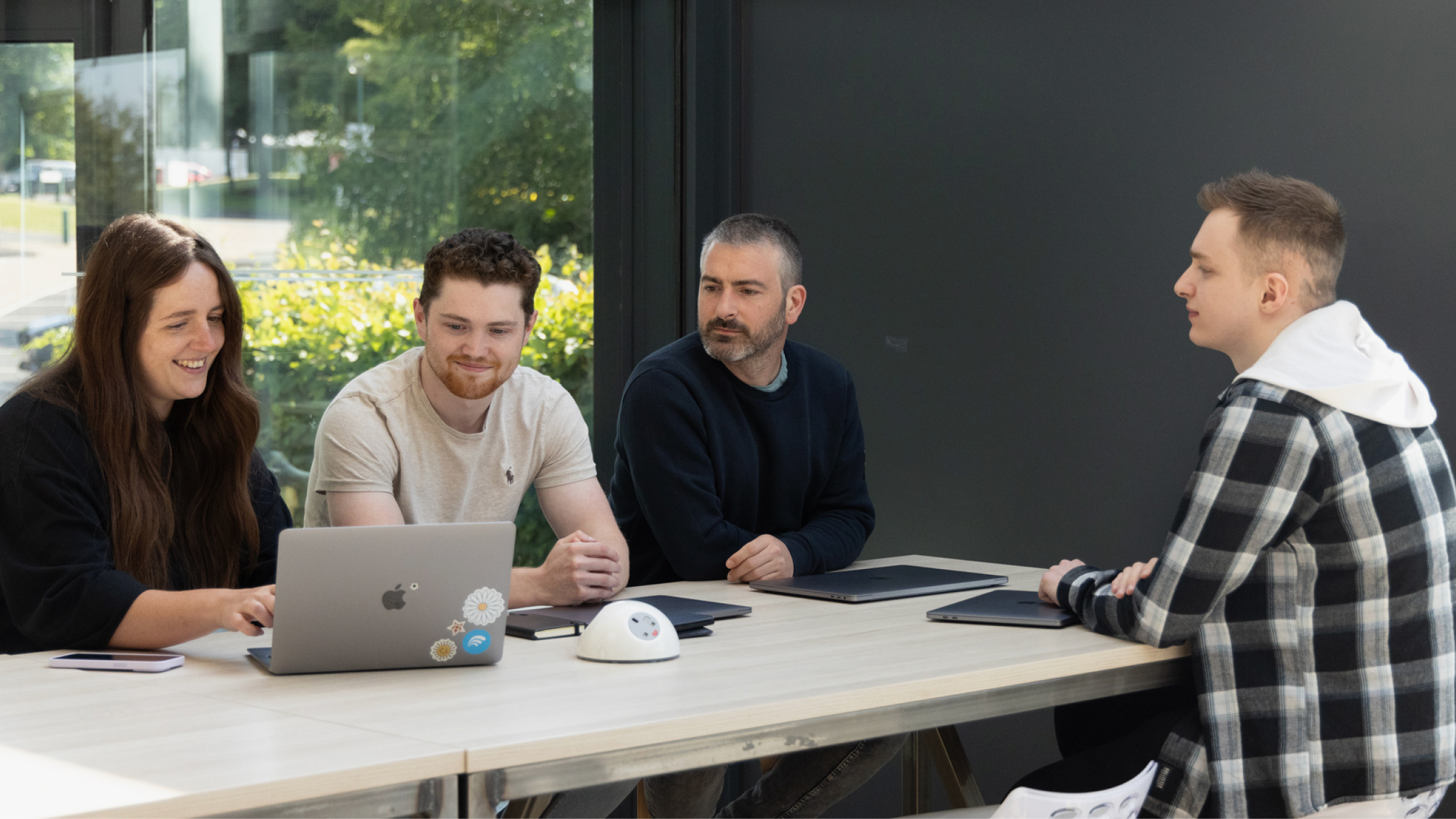 A web development team sitting at a desk and reviewing work together, set in a contemporary web design agency setting.