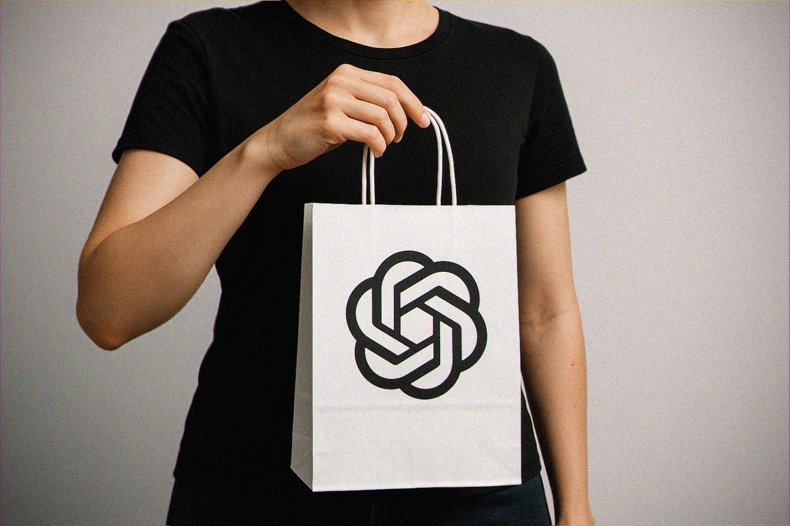 A female with black t-shirt holding a shopping back that has the OpenAI logo on it